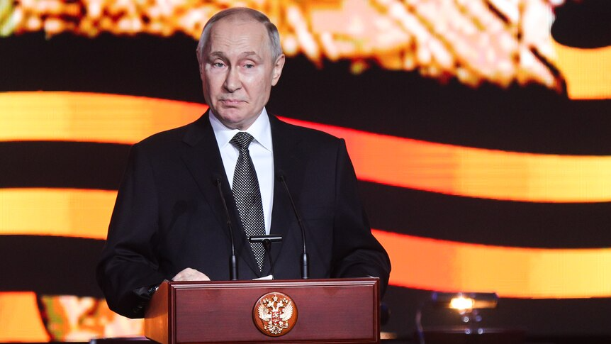 Vladimir Putin stands at a podium.