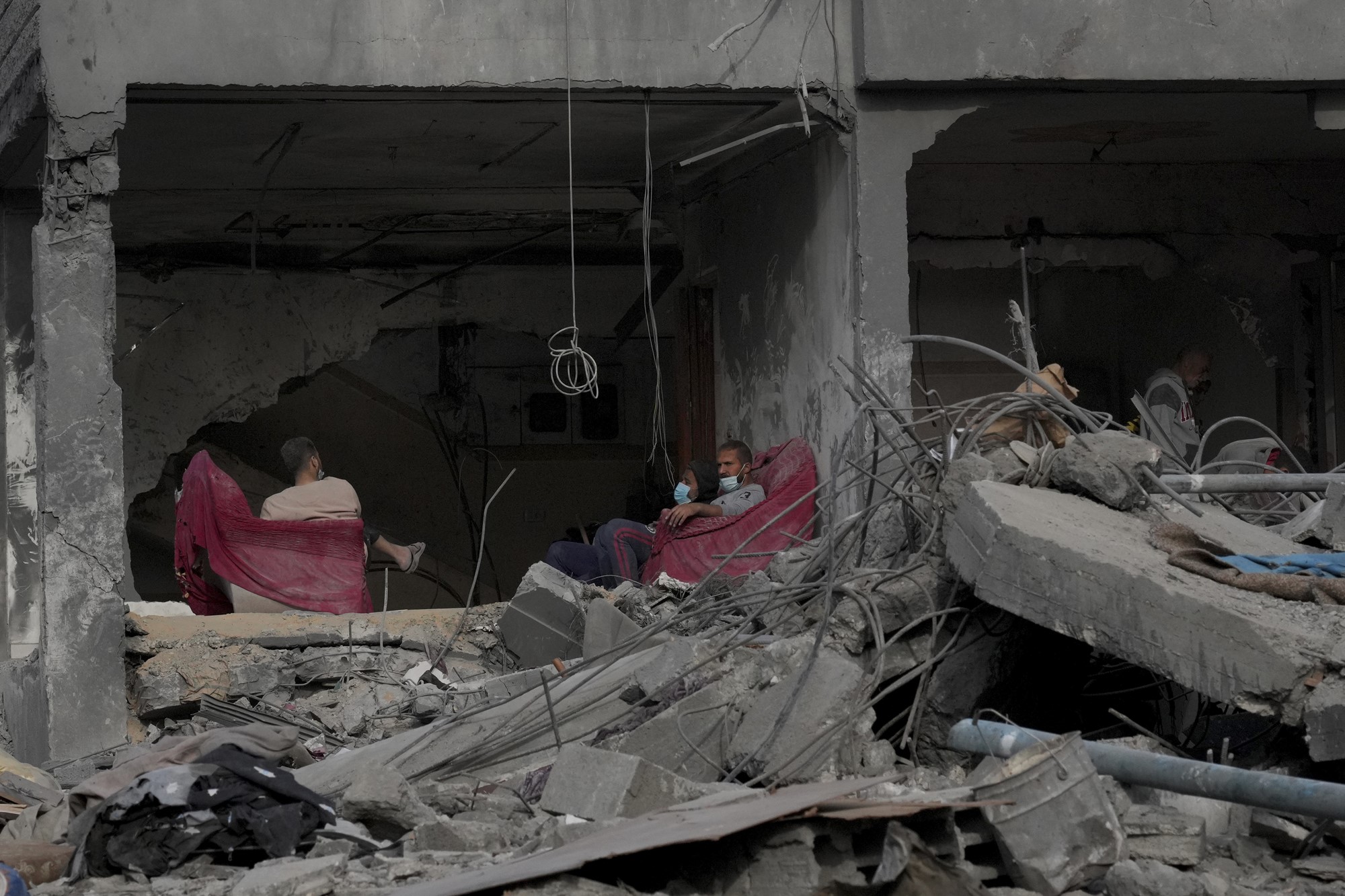 Palestinians sit amid rubble on red chairs 
