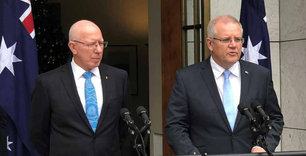 Two men in suits and blue ties stand behind microphones.