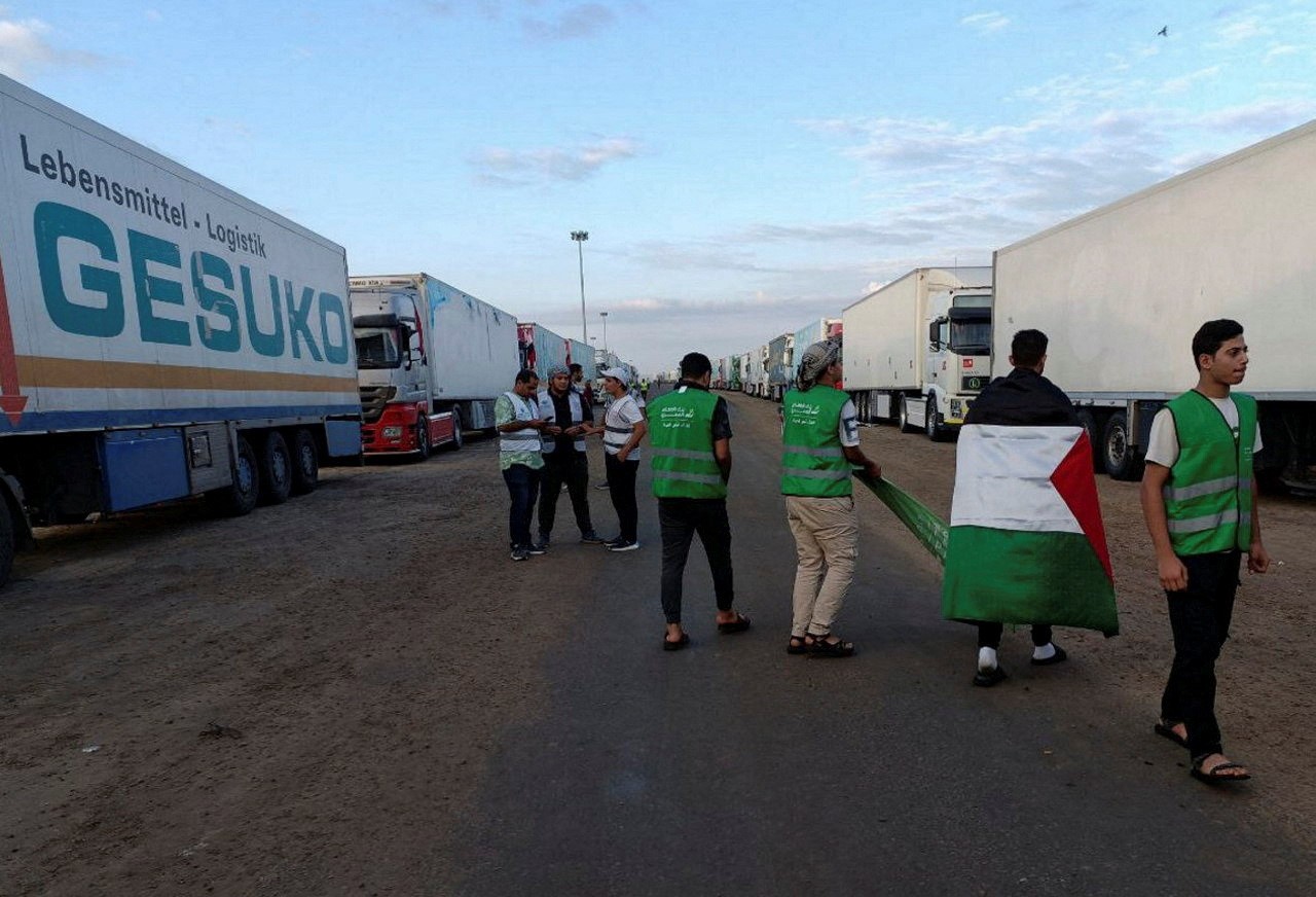 gyptian volunteers gather with a Palestinian flag next to a truck convoy carrying humanitarian aid