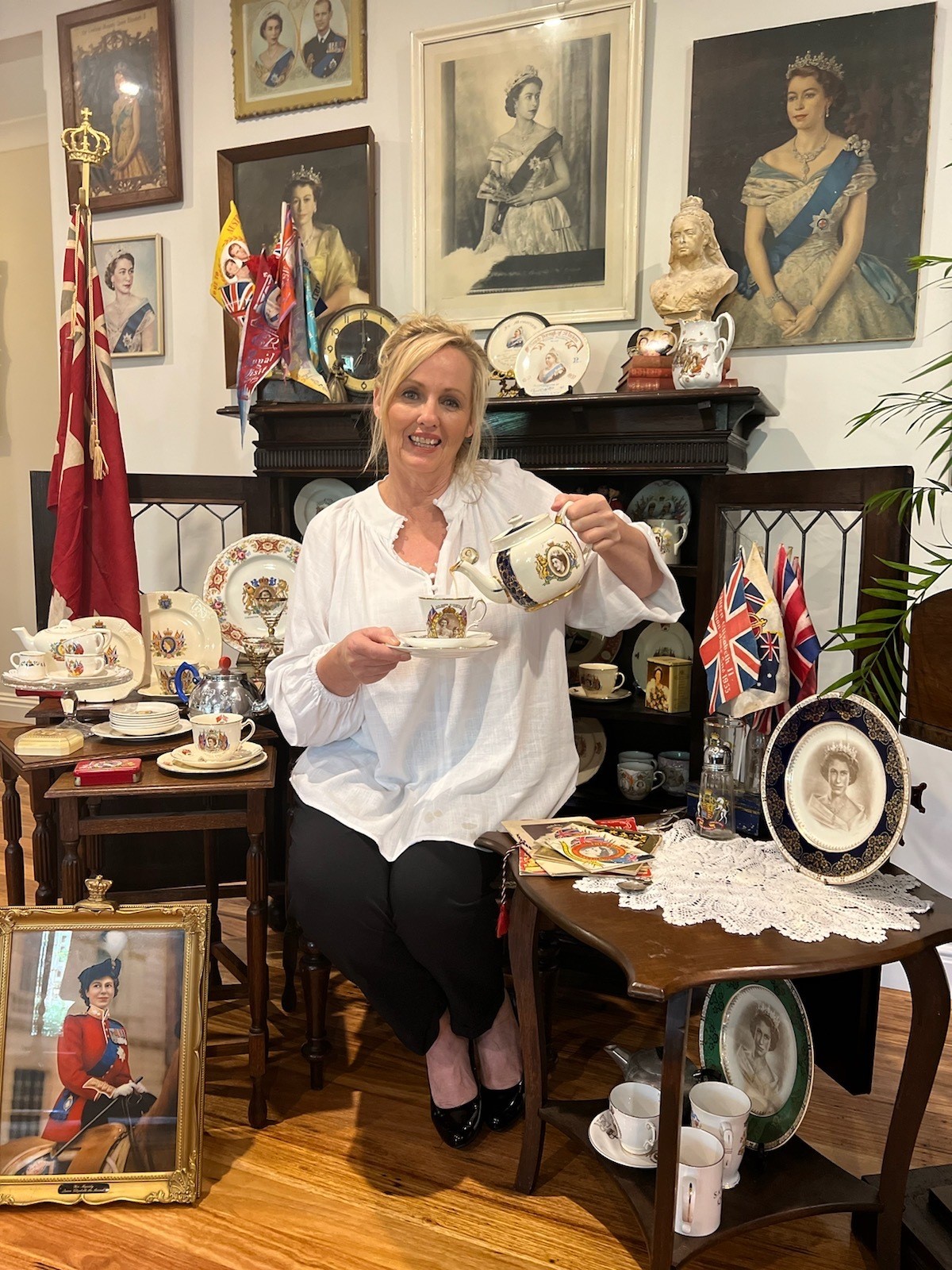 A woman wearing a white shirt sits on a chair pouring a teacup.
