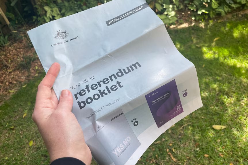 A person holding a Voice to Parliament referendum booklet, which is grey with a federal government logo