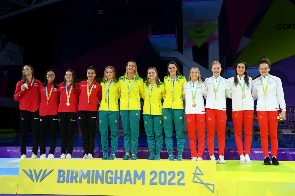 12 swimmers line up with medals on a podium