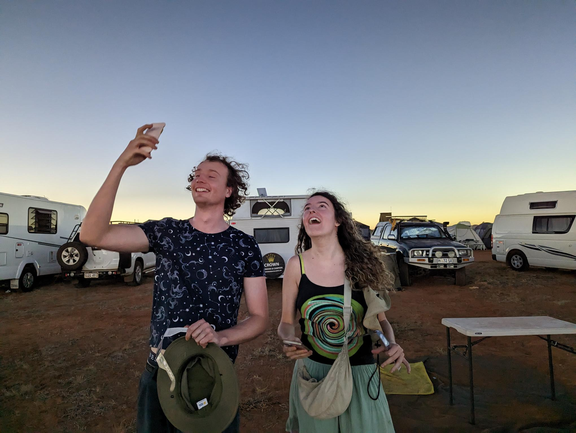 Two young people smile and take photos on their phone.