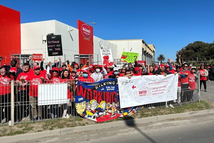 A group of workers gather with banners outside the factory.