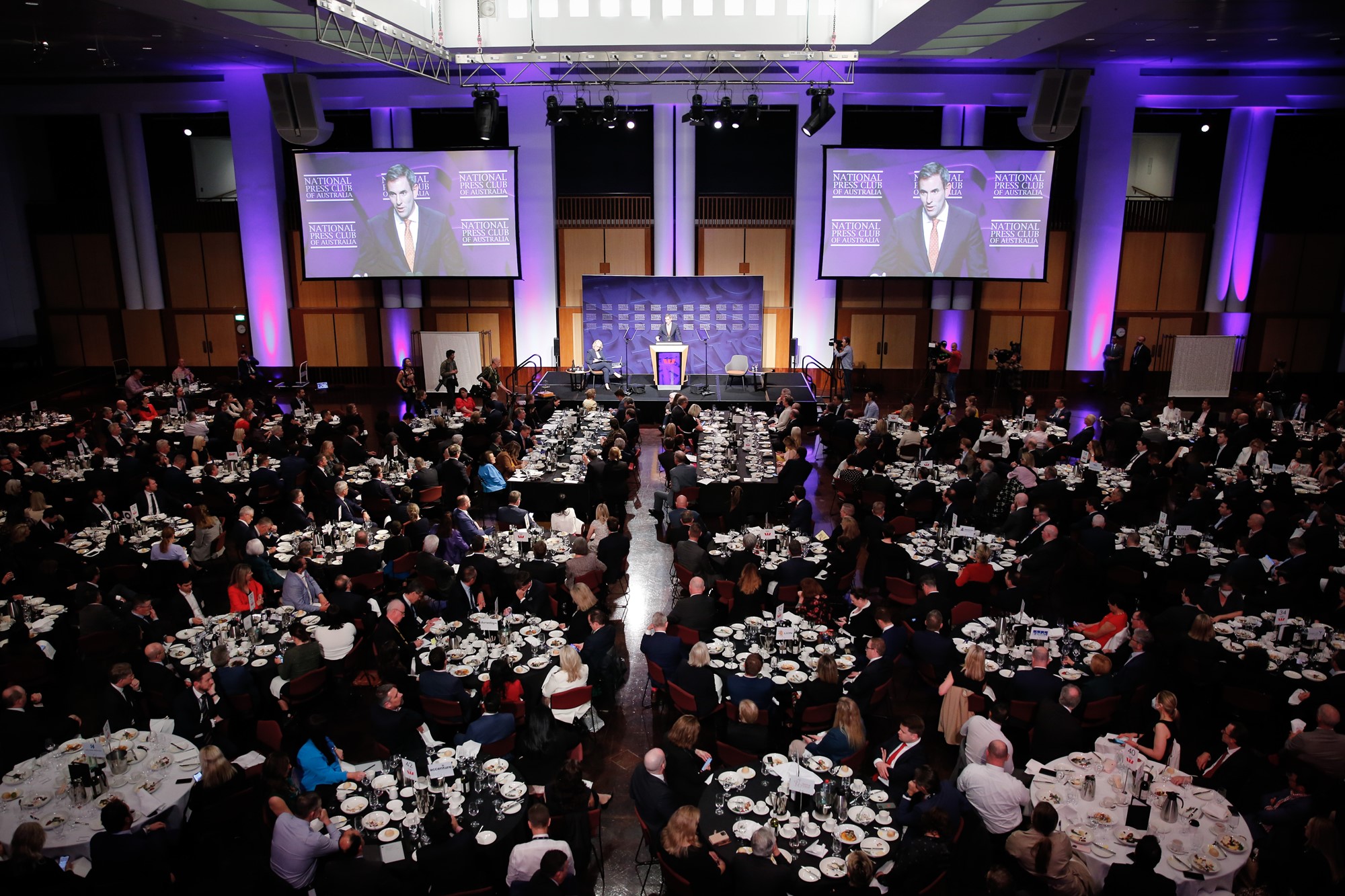 A wide shot of people sitting at round tables while Chalmers speaks.