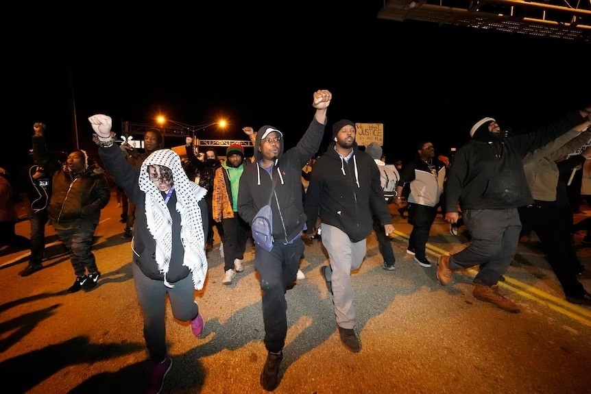 Protesters walk along a road at night holding signs and fists in the air.