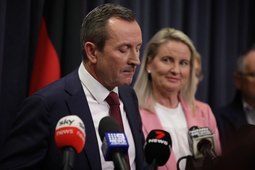 A man shuts his eyes and looks down at a press conference