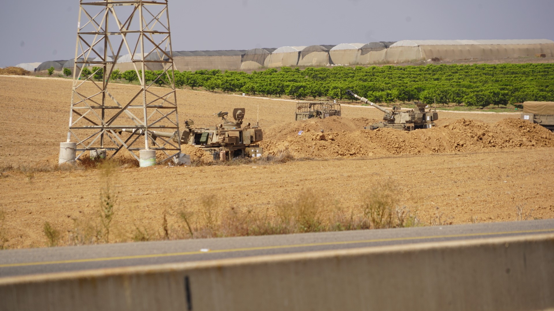 Army vehicles in a field next to a telegraph pole. 