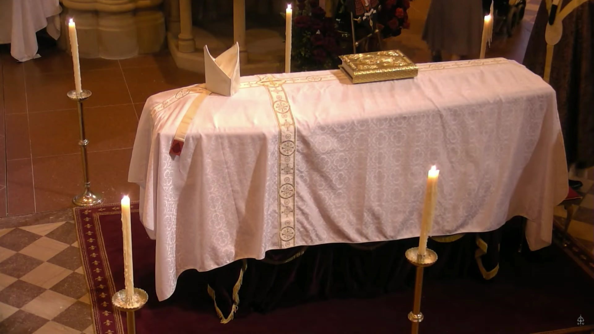 A coffin with a white blanked draped over it and a gold bible on top