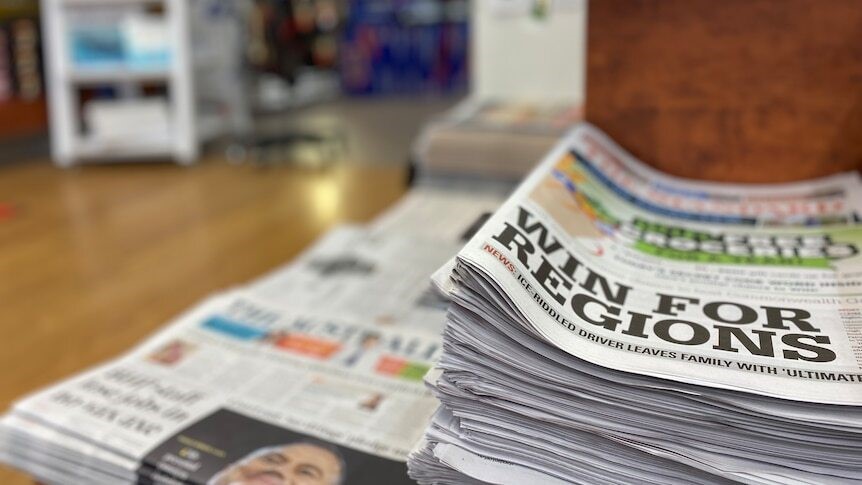 A stack of newspapers with the headline 'Win for Regions' on the top one.