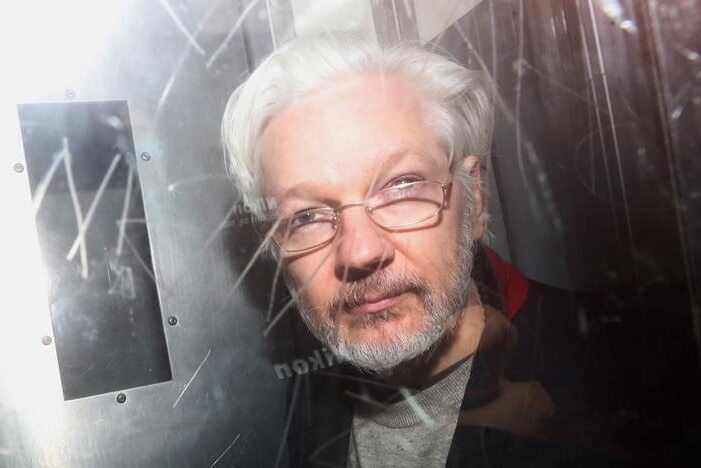 A close up of Julian Assange behind glass.