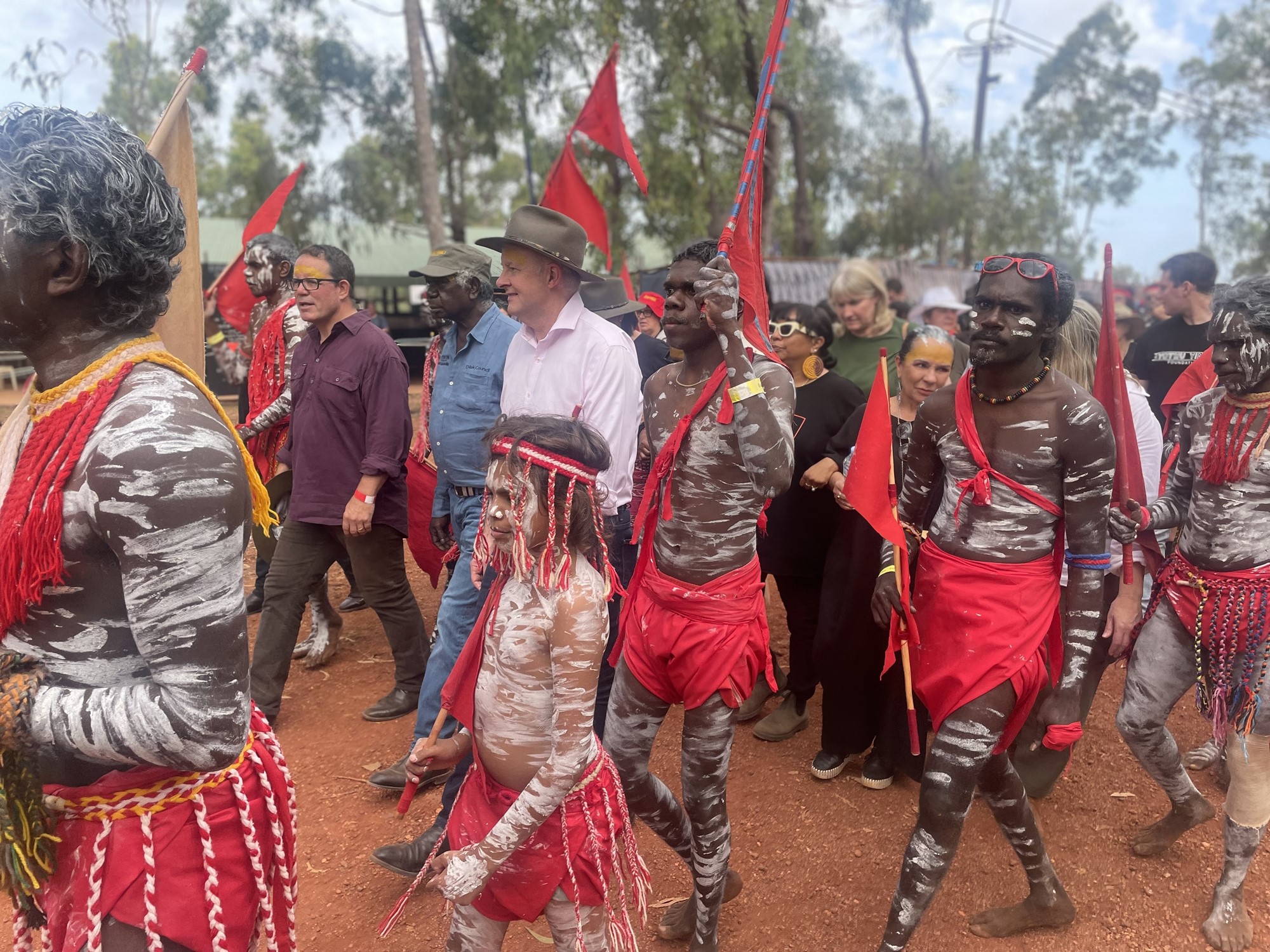 Prime Minister Anthony albanese walks in a crowd of indigenous men in traditional dress