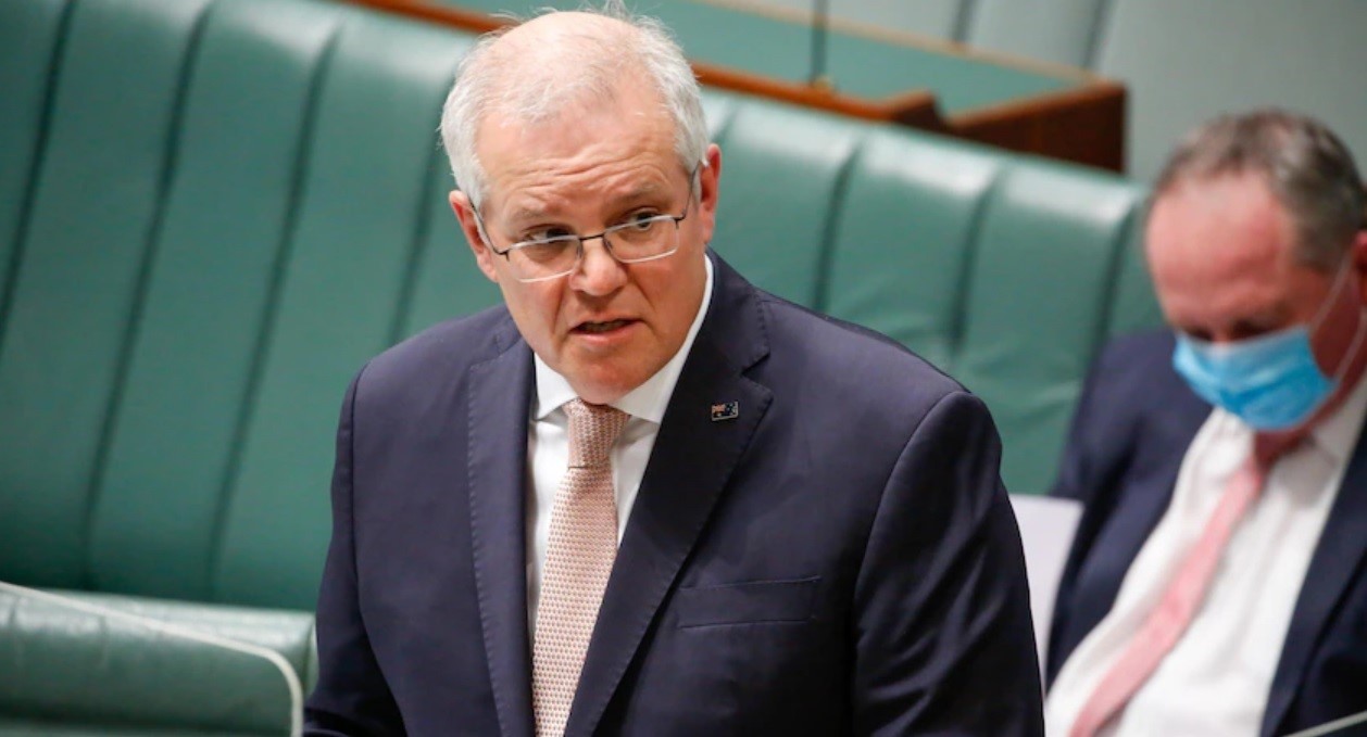 A man in a suit and glasses stands in Parliament.