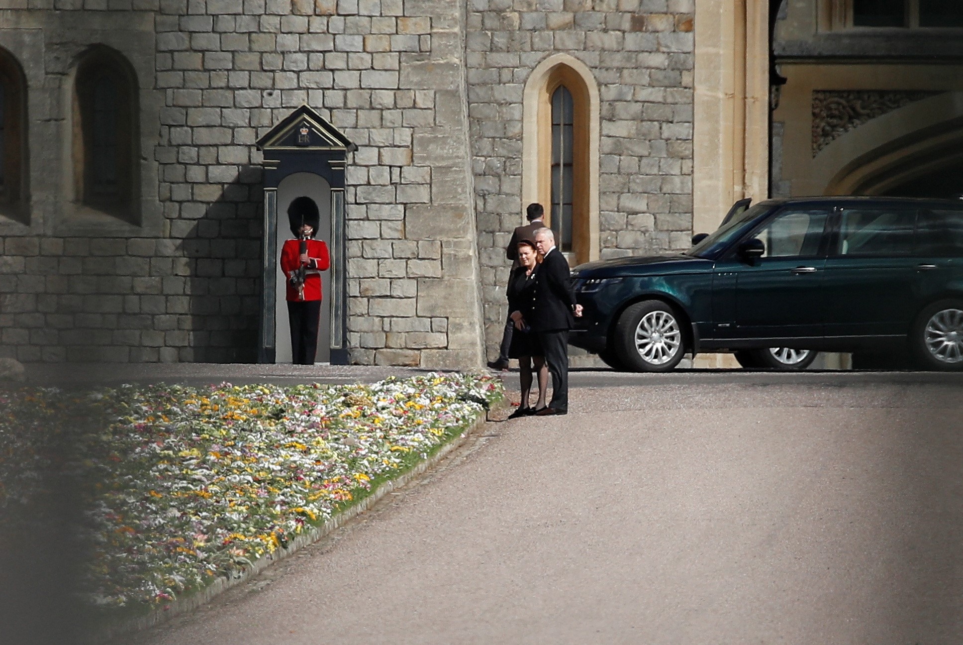 A long shot of the pair, dressed in black, looking at a camera near flowers.