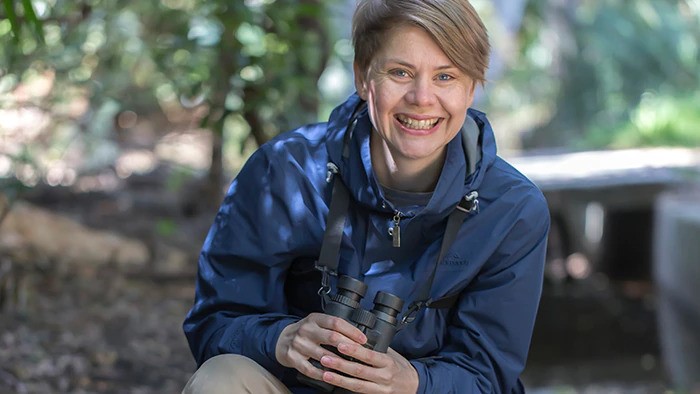 Ann smiles as she bird watches in the forest.