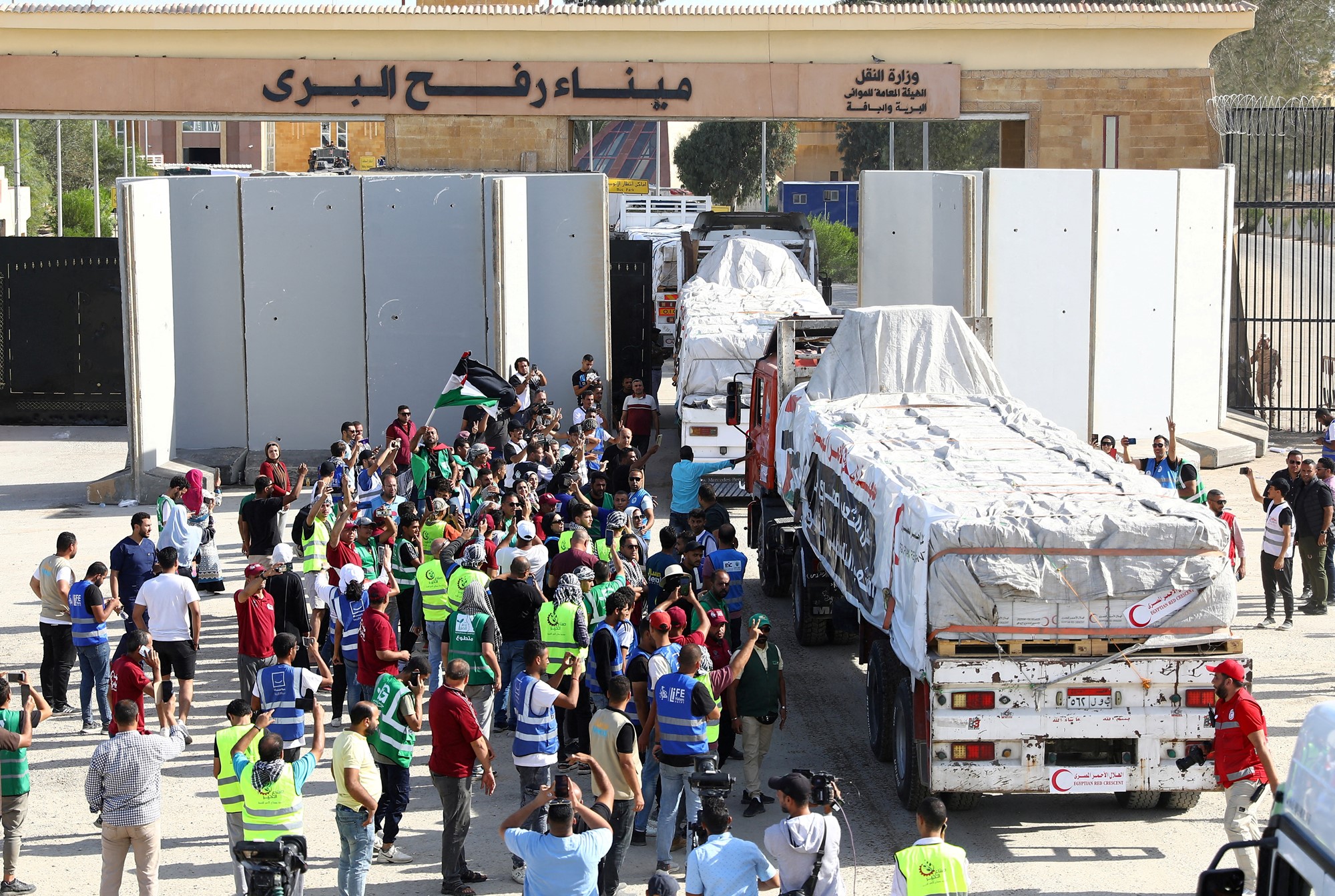 People watch and wave Palestinian flags as aid trucks pass through a border crossing