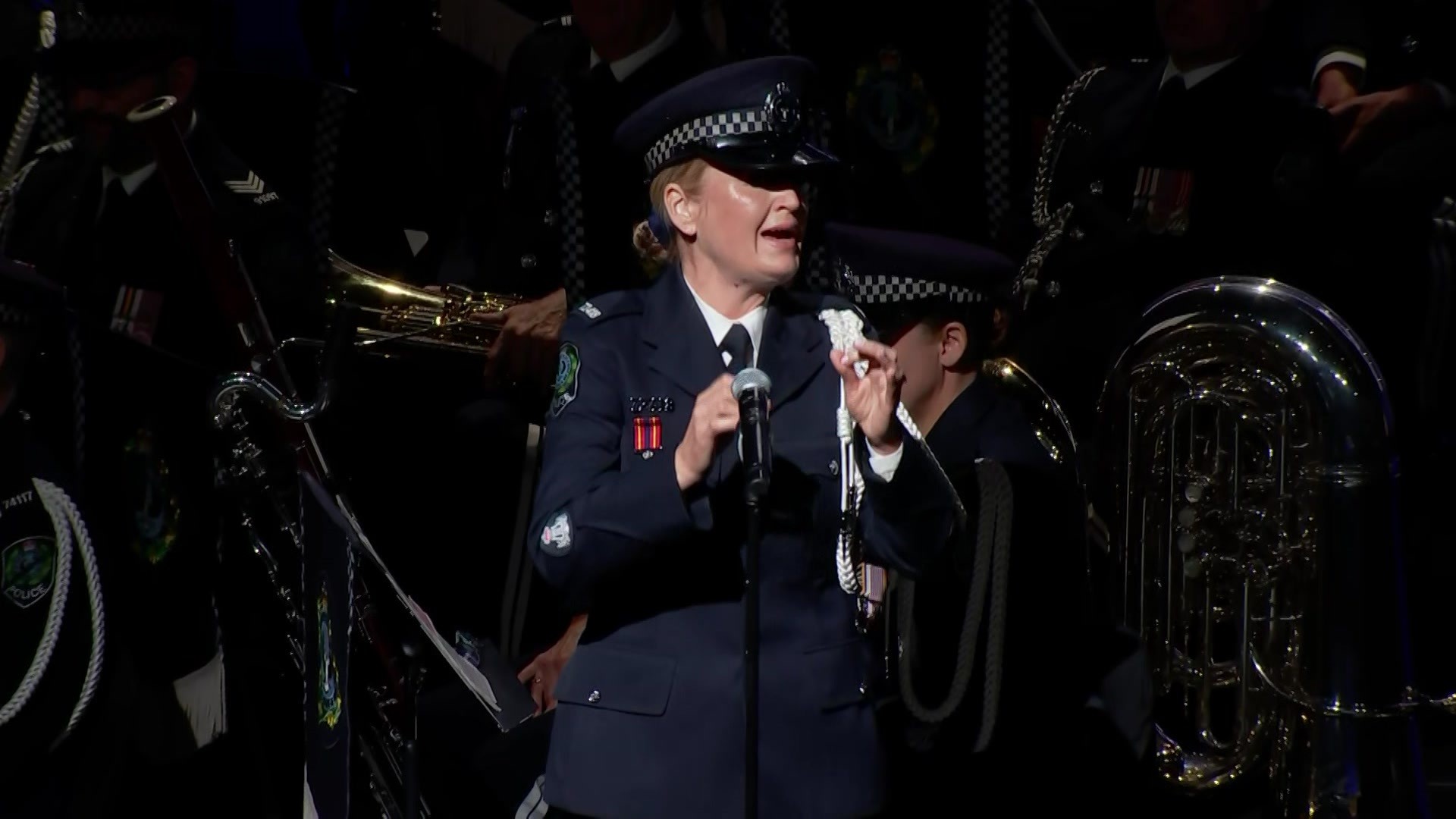 A female police officer sings Amazing Grace on stage at a funeral