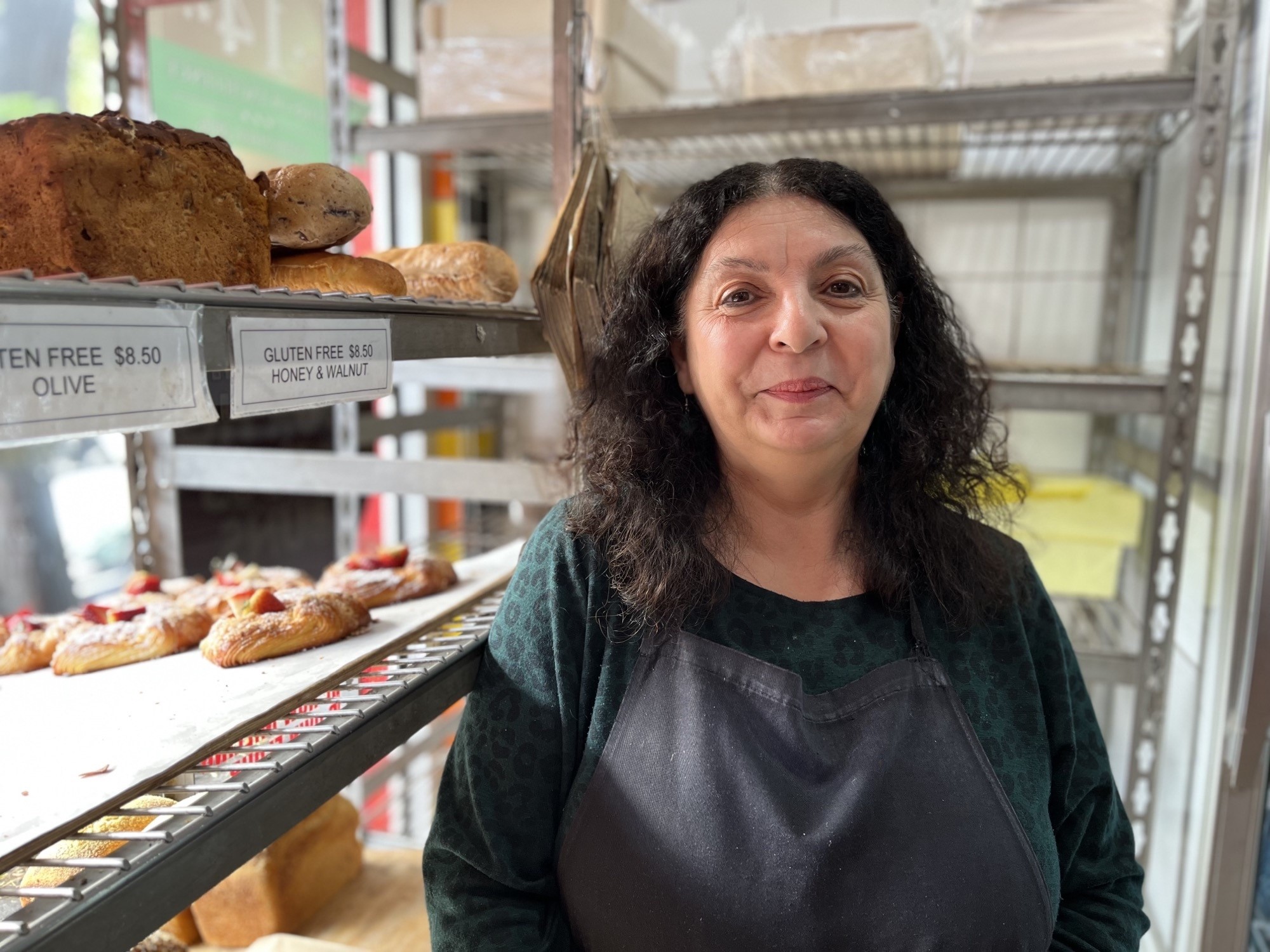 Sandra Cucuzza stands in front of baked goods and smiles for the camera.